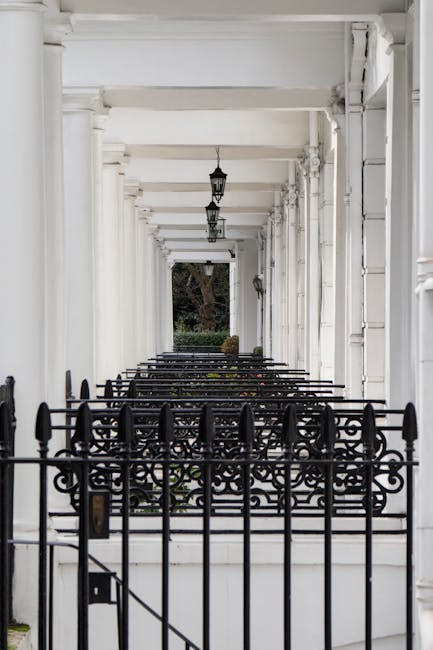 A row of historic red-brick terraced buildings with large sash windows, some featuring wrought iron balconies, situated on a quiet street in South Kensington. The ground-level entrance of the building